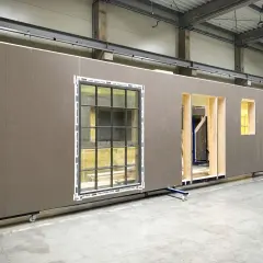 Gotowe ściany drewniane prefabrykowane z oknami i otworami na drzwi, czekające na montaż.