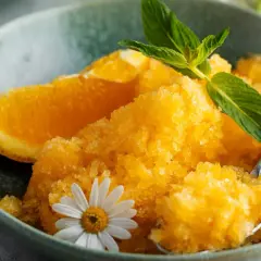 Pomarańczowy sorbet w misce z plasterkiem pomarańczy, miętą i kwiatkiem.