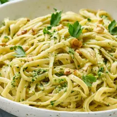 Pasta con pesto cremosa, adornada con nueces y perejil fresco. Un plato italiano delicioso y vibrante.