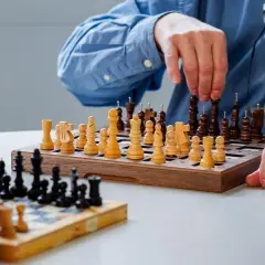 Deux personnes jouent aux échecs. Les pièces ont des ergots pour aider à les identifier, rendant ce jeu accessible aux aveugles.