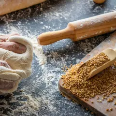 Manos amasando masa para pan de cebada. Granos de trigo en una pala de madera sobre una tabla.