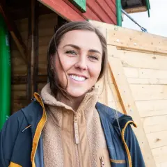 Amanda Robinson ler glatt framför en grön surfbräda och en träbyggnad.