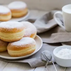 Bomboloni alla crema spolverati di zucchero a velo, pronti per essere gustati con una tazza di latte.