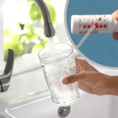 Biała woda z kranu leje się do szklanki. W tle test paskowy do wody pokazuje dobre wyniki.