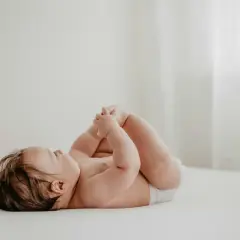 Un neonato con un adorabile culetto rosso, sdraiato su un lettino, gioca con i suoi piedini.