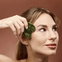 Kobieta wykonuje masaż twarzy kamieniem gua sha, by uzyskać promienny wygląd. Widoczne gua sha efekty.