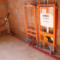 Instalacja hydrauliczna przed tynkami: stelaże podtynkowe, rury i spłuczka JomoTech w budowie.