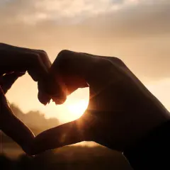 Dłonie tworzą serce na tle zachodzącego słońca. To piękny symbol miłości, ale czasem może być to też początek love bombingu.