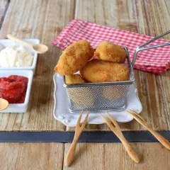 Croquetas de gambas doradas y crujientes en una cesta metálica, acompañadas de ketchup y mayonesa.