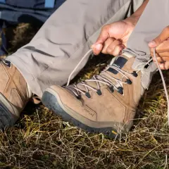 Ręce zaciskają sznurówki brązowego buta trekkingowego. Solidna podeszwa buta zapewnia przyczepność na nierównym terenie.