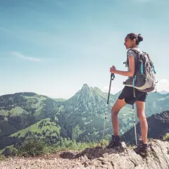 Młoda kobieta z plecakiem i kijkami trekkingowymi podziwia panoramę gór. Idealny widok dla tych, którzy zastanawiają się, jak zacząć chodzić po górach.