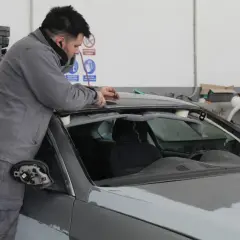 Taller mecánico. Un hombre trabaja en el techo de un coche gris, solucionando stage 1 problemas.