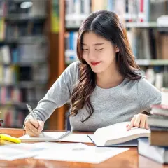 Młoda kobieta studiuje w bibliotece, otoczona książkami. Jej skupienie i lekki uśmiech sugerują, że pokonuje wszelki sceptycyzm w drodze do wiedzy.