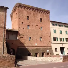 Torre medievale in mattoni a Monteroni d'Arbia, con edifici adiacenti in pietra e intonaco.