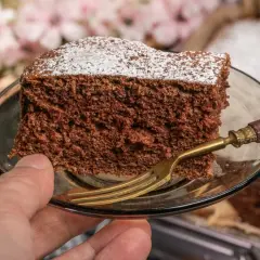 Kawałek najprostszego ciasta czekoladowego, posypana cukrem pudrem, na talerzyku z widelcem.