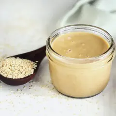 Un vasetto di tahina, crema di sesamo, accanto a un cucchiaio di semi. Scopri cos'è la tahina e come usarla.