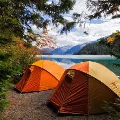 Dwa pomarańczowe namioty na brzegu jeziora, otoczone jesiennymi drzewami. Idealne miejsce na camping Jastrzębia Góra.