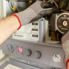 Ręce w rękawiczkach pracują przy budowie bojlera elektrycznego, regulując pompę Grundfos.