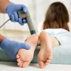Thérapeute appliquant des ondes de choc sur le pied d'une patiente. Bien que souvent bénéfique, il faut connaître les inconvénients des ondes de choc.