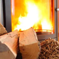 Cheminée avec un feu vif. À gauche, des bûches de bois. À droite, un tas de granulés. Un insert mixte bois et granulés, avis sur le rendement.