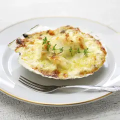 Deliciosas vieiras gratinadas en su concha, cubiertas de queso derretido y doradas, adornadas con una ramita de tomillo.