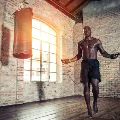 A muscular boxer practices how to jump rope like a pro in a brick gym, with a punching bag nearby.
