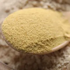 Une cuillère en bois remplie de levure de bière en poudre, jaune pâle. La question "la levure de bière fait elle grossir ?" plane.