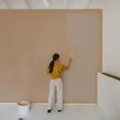 Frau streicht Wand mit neuer Farbe. Die Frage, wie lange braucht Wandfarbe zum trocknen, beschäftigt sie.
