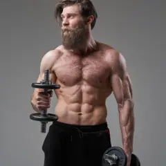 Mężczyzna z imponującą brodą wykonuje ćwiczenia na biceps, trzymając hantle do hammer curls.
