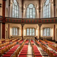 Innenraum einer epo church mit vielen roten Stuhlreihen und großen Bogenfenstern. Ein Mann sitzt allein.