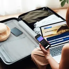 Karta kredytowa z ubezpieczeniem podróżnym w ręku, obok walizki i laptopa z rezerwacją lotów.