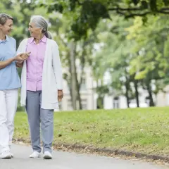 Pflegekraft stützt ältere Dame, die wegen Demenz weglauftendenz hat. Hilfsmittel wie diese Spaziergänge sind wichtig.