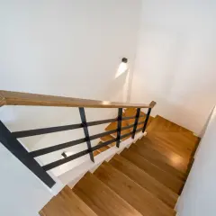 Nowoczesne oświetlenie klatki schodowej w domu jednorodzinnym, z drewnianymi stopniami i czarną balustradą.