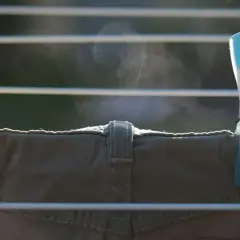 Zwei Wäscheklammern, gelb und blau, halten eine Hose auf einer Wäscheleine. Dampf steigt auf, die Hose trocknet schnell.