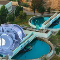 Un compresor de lóbulos Howden en primer plano, con una planta de tratamiento de agua al fondo.