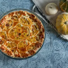 Torta salata zucca salsiccia e stracchino, con decorazione a intreccio e ripieno dorato. Accanto, zucche decorative.