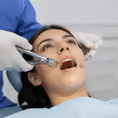 Dentista usa fórceps para sacar muelas a paciente con boca abierta.