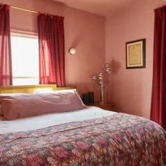 A bedroom with a large bed covered by a colorful quilt. Red curtains hang beside the bed, effectively creating a cozy nook and demonstrating how to hide a window behind a bed.
