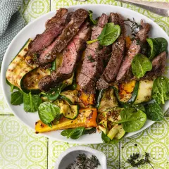 Pokrojony, soczysty sirloin steak z grillowanymi warzywami: cukinią, papryką i szpinakiem, udekorowany świeżym tymiankiem.