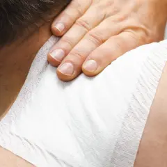 Dłoń uciska plaster przeciwbólowy na karku, przynosząc ulgę w bólu.