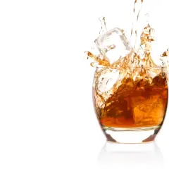 Bursztynowa whisky z lodem rozpryskuje się w szkle. Czy whisky podnosi ciśnienie? To pytanie pozostaje otwarte, gdy patrzymy na ten dynamiczny obraz.