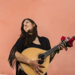 Młoda kobieta z gitarą, ozdobioną czerwonymi różami, przypomina duchem Amalię Rodrigues, legendę fado.