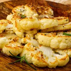Tranches de chou-fleur rôti, dorées et garnies d'herbes, servies sur un plat en bois.