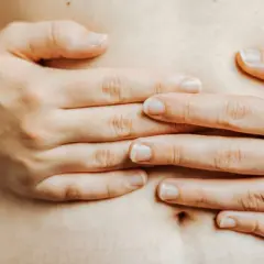 Mains d'une femme sur son ventre, évoquant la constipation et la pression sur la vessie.