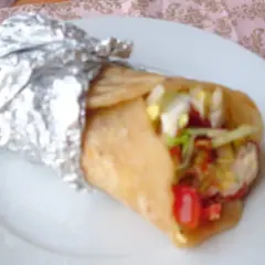 Pyszny placek z kebabem, zawinięty w folię aluminiową, z widocznym nadzieniem z warzyw i mięsa.