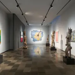 Osman Can Yerebakan's exhibition features striking wooden sculptures and vibrant paintings in a modern gallery space.