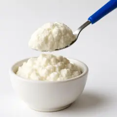 Ricotta fresca in una ciotola, con un cucchiaio che ne preleva una porzione. Un alimento leggero, ideale per chi controlla il colesterolo.