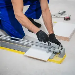 Ręce w rękawiczkach precyzyjnie tną gres 2 cm na płytkarskiej przecinarce.