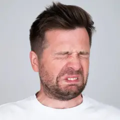 Mężczyzna z wykrzywioną twarzą, oczy zamknięte, czuje gorzki smak w ustach.