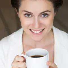 Uśmiechnięta kobieta z filiżanką kawy, jej codzienna dawka kofeiny dodaje energii.